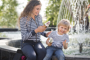 Fototapeta na wymiar Cute little boy and his mother staining each other with ice cream near the fountain outdoors. Young pretty mom and her son having fun together