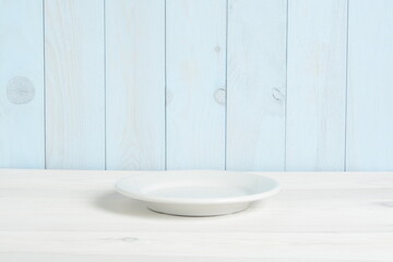 Plato blanco vacío en mesa de madera blanca y pared azul