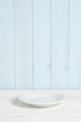 Naklejka na ściany i meble Plato blanco vacío en mesa de madera blanca y pared azul