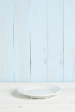 Plato blanco vacío en mesa de madera blanca y pared azul