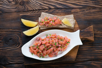White plate with salmon tartar in a rustic wooden setting, flat-lay, horizontal shot