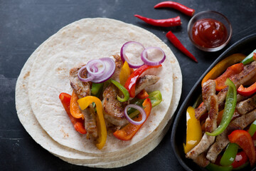 Wheat wraps filled with mexican pork fajitas, dark metal background, studio shot