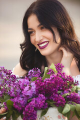 Beautiful girl outdoors. Pretty young woman with bouquet of lilac. Lady with flowers close up