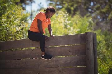 Determined woman climbing wooden wall during obstacle course