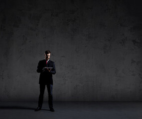 Businessman standing with computer tablet over dark wall background. Business, career job concept.