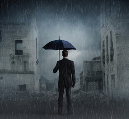 Businessman with umbrella standing over apocalyptic background. Crisis, default, setback concept.