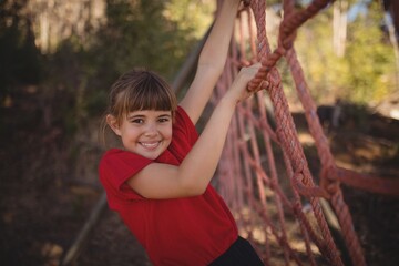 Portrait of happy girl climbing a net during obstacle course