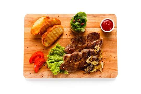 Grilled steaks and vegetables on cutting board on white background