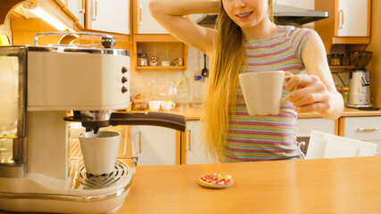 Woman in kitchen making coffee from machine