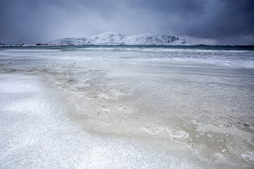 Waves of the icy sea on the beach in the background the snowy peaks Ramberg Lofoten Islands Norway Europe