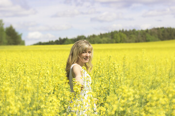 Naklejka na ściany i meble Woman with long hair, yellow rapeseed canola field enjoying nature and sunlight.