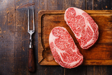 Raw fresh marbled meat Steak Ribeye Black Angus and meat fork on wooden background copy space - obrazy, fototapety, plakaty