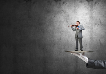 Businessman on metal tray playing violin against concrete background