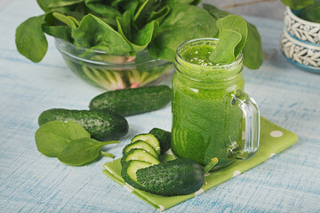 Green spinach and cucumber smoothie on light blue wooden background.