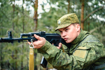 Fototapeta premium Portrait of a Russian soldier in modern military uniforms and weapons, machine gun. Green form on the background of a pine forest