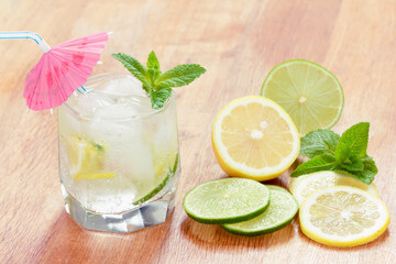 A glass of cold water with lemon and lime, ice cubes and mint leaves