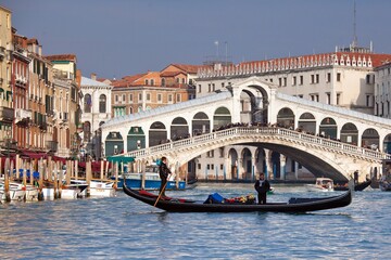 Fototapeta na wymiar A gondola crossing the Grand Canal right in front of the Rialto Bridge, one of the most recognizable Venetian landmarks Venice, Veneto Italy Europe