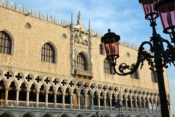 Fototapeta na wymiar The faÃ§ade of the Doge's Palace including a lower section consisting of a ground floor colonnade beneath an open loggia. In the foreground a typical Venetian lamp post, Venice, Veneto Italy Europe