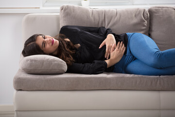 Woman Lying On Couch Having Stomach Ache