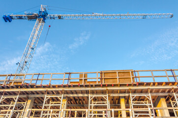 High-rise building under construction. The site with crane against blue sky with white clouds.