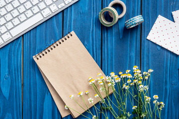 colorful work space with keyboard, notebook and flowers for home office blue wooden background top view mockup