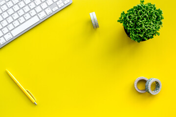 home office desk with plants, sticky tape and keyboard on yellow background top view mock up