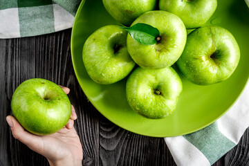 summer food with green apples in plate on dark background top view