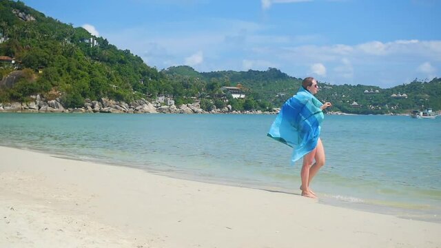 a young girl with a pareo is along the shore of the beach. Tropical island, the warm summer wind
