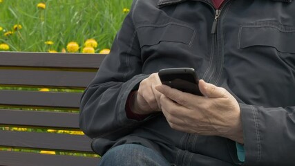 Elderly Man Sitting On Park Bench And Messaging On Mobile Phone