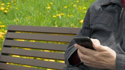 Elderly Man Sitting On Park Bench And Messaging On Mobile Phone