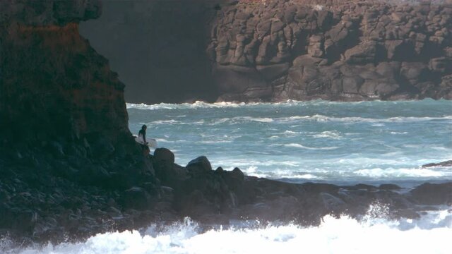 Surfer walking along the coastal rocks carrying a broken surfboard