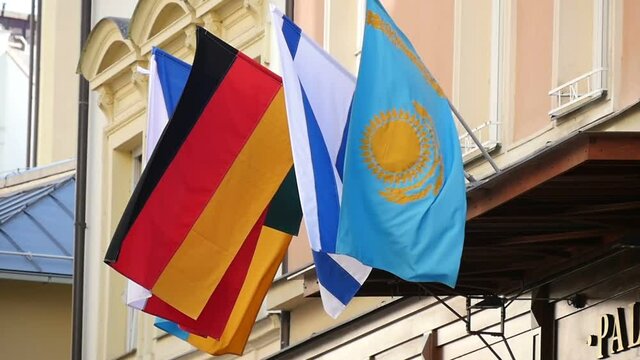 Original down up view on state flags of Kazachstan, Israel, Germany,  Romania and Czech republic, hanging over the entrance of some official building in Prague in a sunny day in slow motion