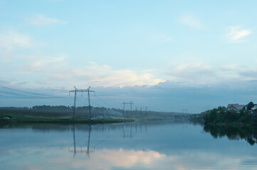 Evening misty landscape of the countryside. The river is in a fog. Wires of electric voltage.