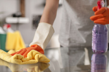 Woman in gloves cleaning table with spray.
