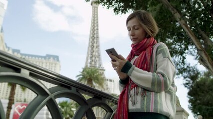 Young gorgeous woman is texting while standing on a sidewalk in Las Vegas with the Eiffel tower on a background