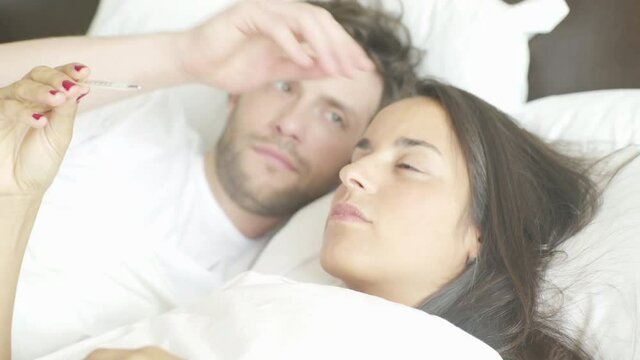 Woman lying in bed taking temperature with thermometer