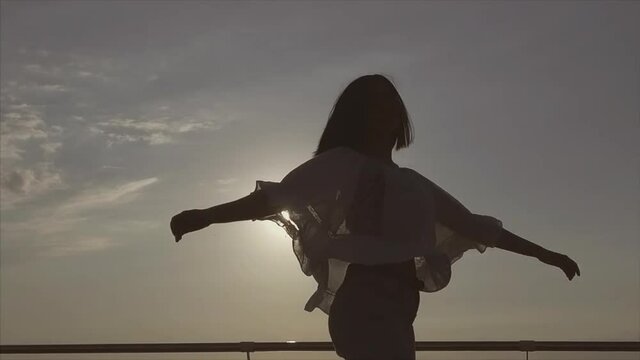 The spinning around woman in white beautiful blouse on sunrise background near sea or ocean. Happiness concept. Slow motion.