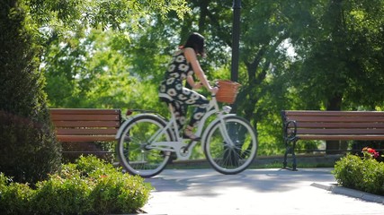 Young girl wearing black overalls with sunflowers on old style italian bicycle with back light. Close up of girl feet riding vintage bike outdoor for spring time. Vintage fashion concept. Slow motion. - Powered by Adobe