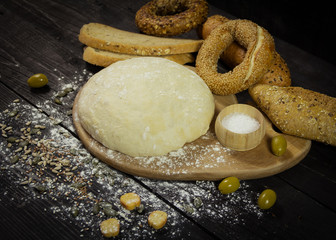 Dough on a wooden board with snacks set and olives in the background