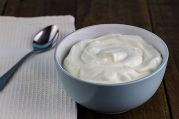 Natural yoghurt in bowl with spoon on rustic wooden table background
