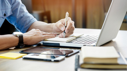 Young business man working in bright office, using laptop, writing notes.