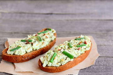 Vegetarian sandwich recipe with guacamole. Open rye sandwiches with avocado guacamole, fresh green onion and spices on a paper and a vintage wooden background with copy space for text
