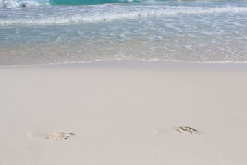 Footprints in the sand on a white sand beach.
