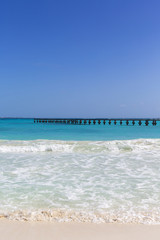 White sand beach. The shore of the Caribbean sea. Long wooden pier in the sea. Turquoise waters. Calm scenery. Vacation concept image. Copy space.