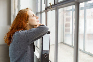 frau stützt sich nachdenklich auf einen aktenordner und schaut aus dem fenster