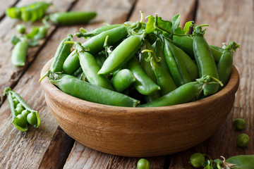 Fresh green peas in a bowl on a wooden background