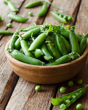 Fresh green peas in a bowl on a wooden background