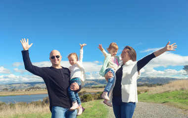 Happy family of four outside with arms in the air