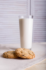 Chocolate biscuits and a glass of milk on a linen towel on a wooden table with a white background. Vintage view. Place for the inscription.