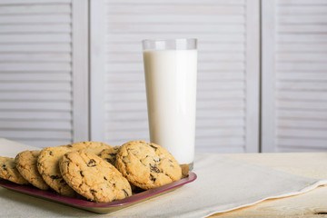 Chocolate biscuits and a glass of milk on a linen towel on a wooden table with a white background. Vintage view. Place for the inscription.